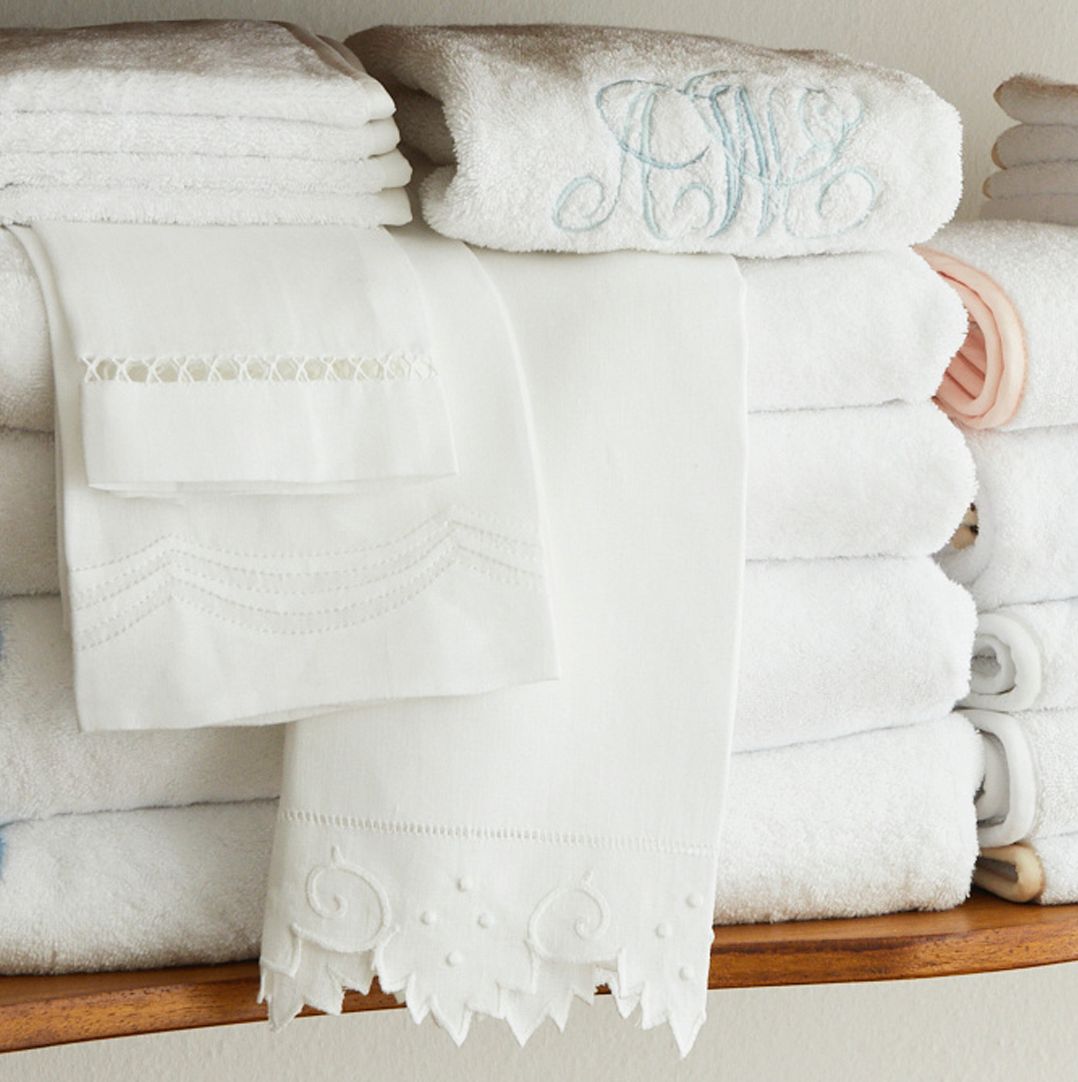 Stack of folded white towels with embroidered details on the edge, displayed on a wooden shelf.
