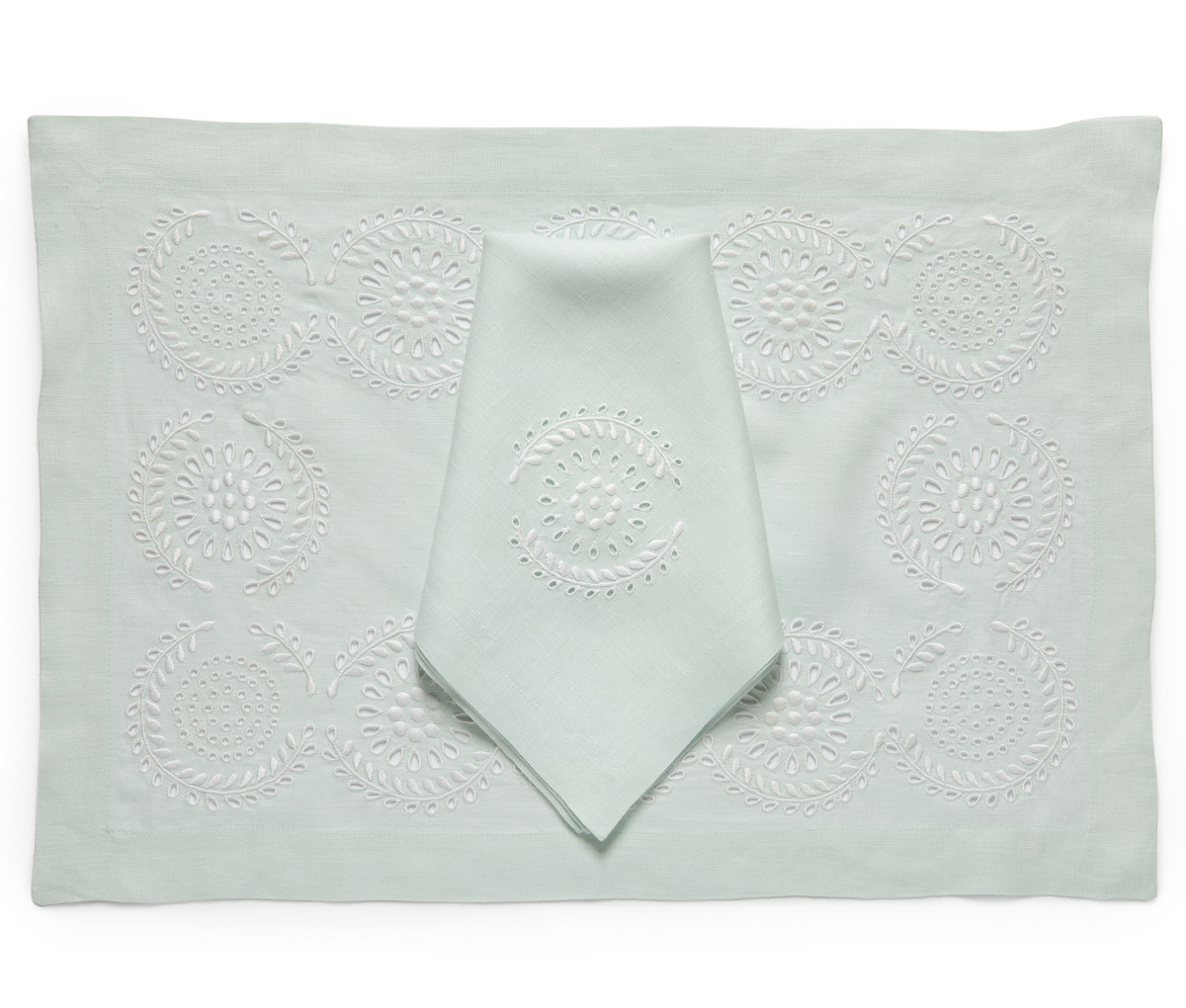 A pale mint green embroidered table linen set featuring a rectangular placemat with a matching folded napkin, both detailed with white floral eyelet embroidery, set against a plain white background.